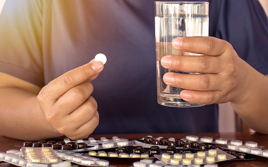 The hand of the patient taking the drug with a glass of water.