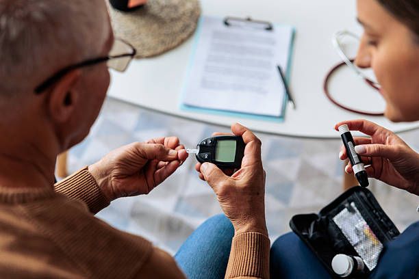 Close-up of a home nurse helping an senior man check his blood glucose level using a glucometer. The image represents home healthcare, diabetes management, and professional medical support for seniors in a comfortable home environment.